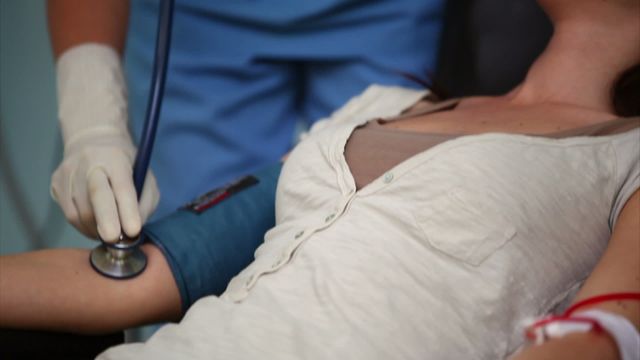 Nurse checks vital signs of a blood donor in a healthcare setting. Useful for health campaigns, clinic brochures, and educational materials focused on blood donation and patient care.