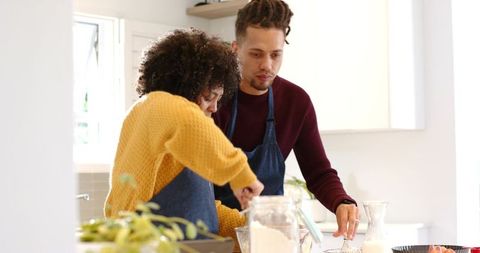 Couple Baking Together in Sunlit Kitchen Wearing Aprons and Cozy Sweaters