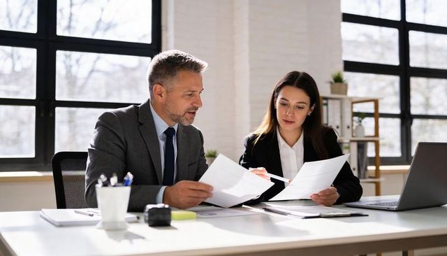Executive Colleagues Reviewing Documents in Bright Modern Office Workspace at Desk