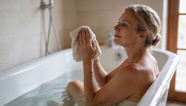 Senior woman enjoying relaxing bath and facial care in bright home bathroom retreat