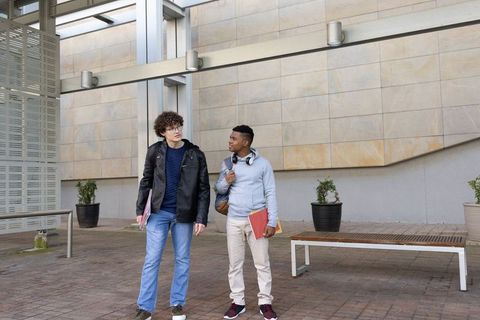 Diverse college students walking through modern campus courtyard carrying folders and backpacks