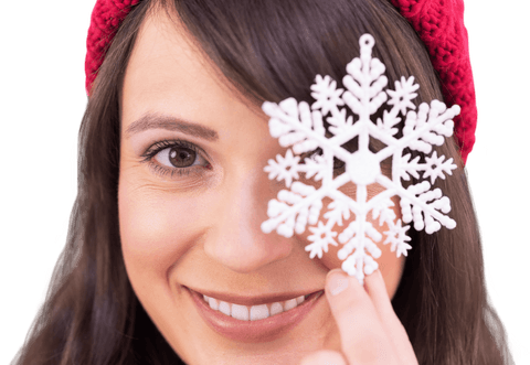 woman wearing red hat, holding snowflake ornament in front of her eye, smiling warmly. perfect for holiday and winter-themed promotions, greeting cards, or festive decoration ideas.