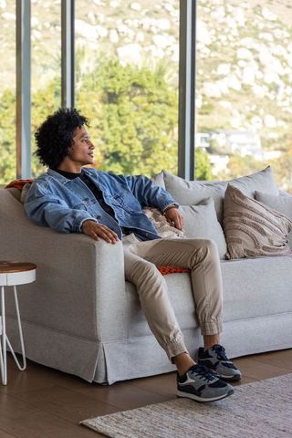 Relaxed african american man lounging on modern sofa by floor-to-ceiling windows