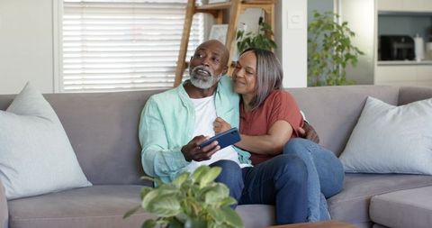 Mature couple cuddling on sofa sharing smartphone in cozy contemporary living room