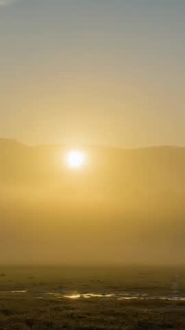Sun rising over ridge with golden mist thinning above reflective marsh, vertical dawn footage