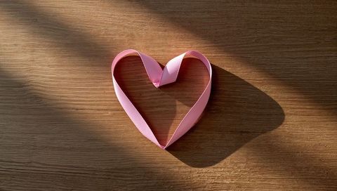 Heart-shaped pink satin ribbon with warm sunlight on wooden surface