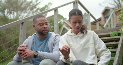 Diverse friends sitting on wooden steps sharing bandage and conversation at cabin retreat