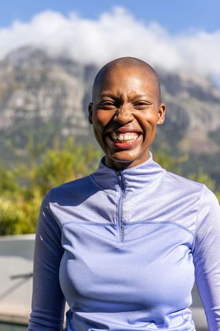 Sunlit smiling african woman standing in lavender quarter-zip top with mountain backdrop