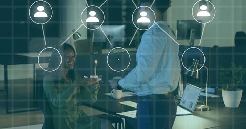 Colleagues celebrating birthday with cupcake and candle, toasting at open-plan office desk