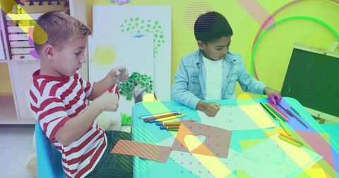 Two Boys Cutting and Drawing at Colorful Classroom Table with Crayons and Scissors