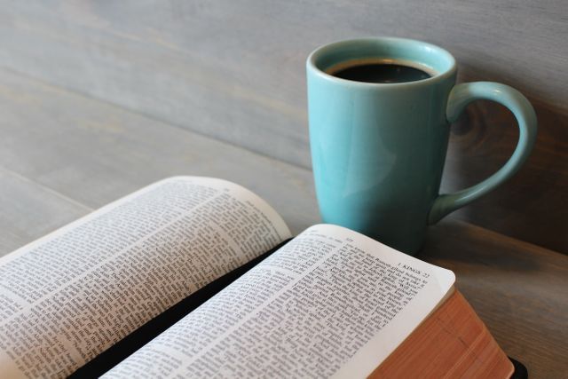 Open Bible with a cup of coffee on a wooden table indicates quiet contemplation or study. Perfect visual for faith-related content, blog articles on Christianity, religious studies, or inspirational social media posts. Highlights alignment of faith and daily routines.