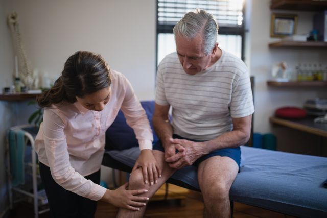 Female therapist examining knee of senior male patient in hospital ward. Useful for healthcare, physiotherapy, elderly care, and medical treatment concepts. Ideal for articles, blogs, and promotional materials related to patient care, rehabilitation, and physical therapy.