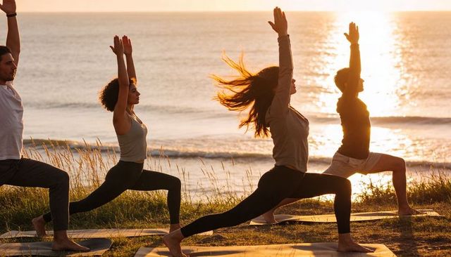 Practicing sunset beach yoga on dune holding warrior i poses barefoot on sunlit mats