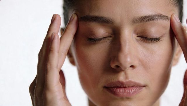 Close-up face portrait pressing temples with fingertips showing skin texture and calm, wellness