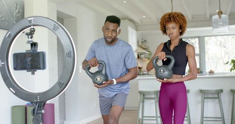 Couple recording home kettlebell workout with ring light and smartphone in kitchen