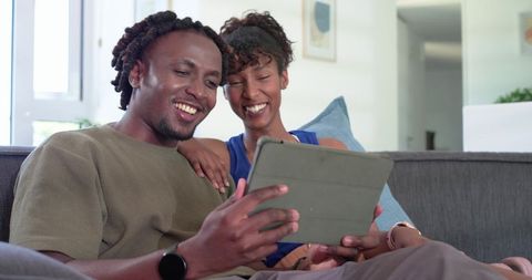 Smiling african american couple relaxing on couch browsing tablet together