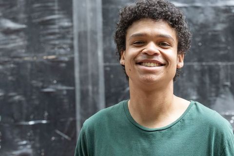 Young man smiling against weathered black wall wearing green t-shirt urban portrait