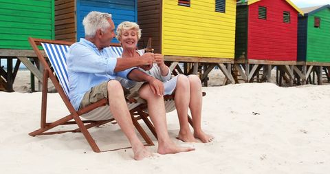 Senior Couple Toasting on Beach with Colorful Huts
