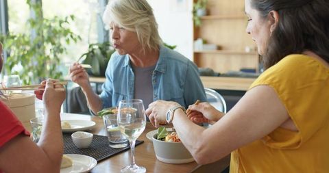 Three women enjoying casual lunch with chopsticks and bamboo steamer at bright dining table