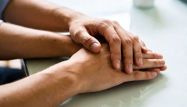 Gentle hands offering comfort and support touching palms on glossy tabletop for care