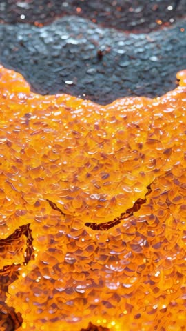 Vertical macro video glowing amber droplets rising and shimmering on dark textured base