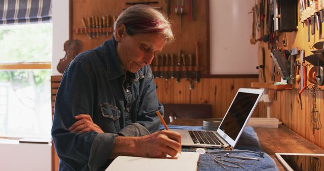 Senior Craftsperson Analyzing Notes in Workshop with Laptop - Download Free Stock Images Pikwizard.com