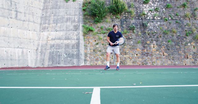 Image of a man playing tennis on an outdoor court, holding a racket. Perfect for illustrating physical activity, sports, fitness, and outdoor recreation. Suitable for articles or marketing materials related to health, exercise, and casual sportswear.