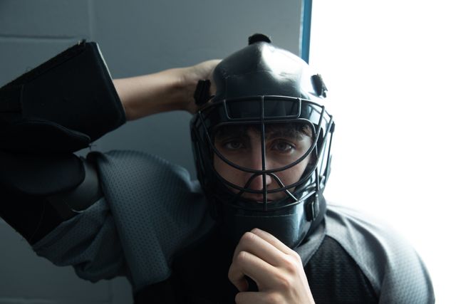 Portrait of Caucasian teenage male field hockey goalkeeper, preparing before a game in the changing room, putting helmet on looking at camera. Sport game competition.