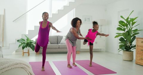 Mother guiding daughters practicing balance yoga on pink mats in bright modern living room