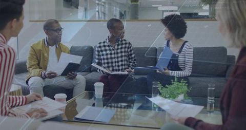 Small team discussing project, reviewing papers and tablets in modern collaborative lounge