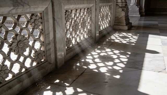 Sunlit marble jali railing casting floral geometric shadows across palace corridor
