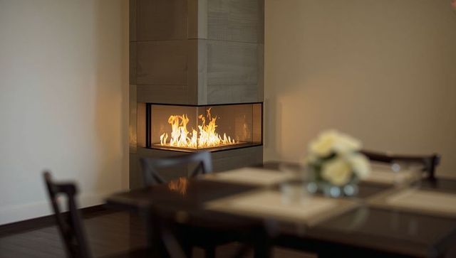 Three-sided corner glass fireplace warming minimalist dining room with rose centerpiece