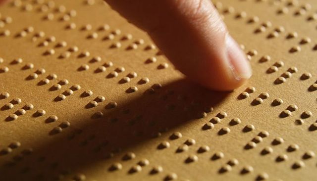 Fingertip tracing braille text on embossed paper under warm light for accessibility