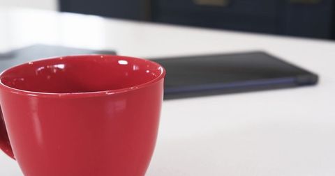 Red Ceramic Mug on Fresh White Kitchen Countertop Near Closed Laptop