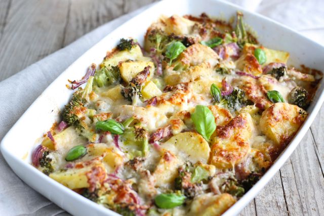 Vegetable and potato casserole with cheese topping shown in white ceramic baking dish. Perfect for use in recipe blogs, healthy eating guides, or promotional material for cooking classes. Appealing for themes like homemade meals, nutritious recipes, and family dinners.