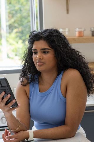 Indian woman checking smartphone while leaning on kitchen counter, modern home lifestyle