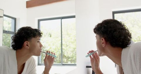 Man Brushing Teeth in Modern Bathroom Wearing Bathrobe