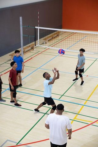 Male indoor volleyball team preparing to receive ball on hardwood gym court