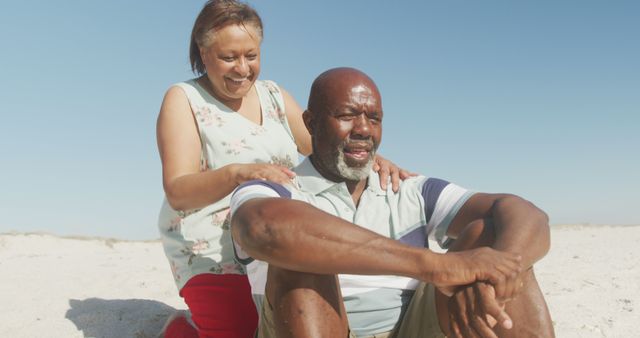 Smiling senior african american couple embracing and looking at sea on sunny beach. healthy, active retirement beach holiday.