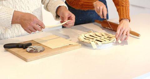 Couple making lattice pie on kitchen counter wearing cozy knit sweaters