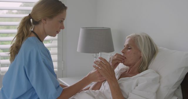 Caucasian nurse assists senior Caucasian woman at home. She provides care and comfort to the elderly patient in a domestic setting.