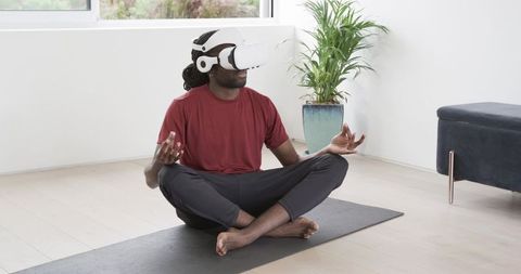 African american man practicing vr meditation on yoga mat in minimalist modern living room