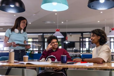 Diverse students collaborating in modern campus lounge around wooden table with tablets