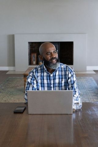 Senior Man Multi-tasking with Laptop and Phone in Cozy Living Room