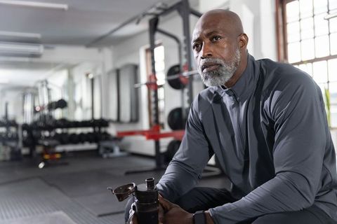 Mature african american man resting at gym bench holding shaker and planning workout