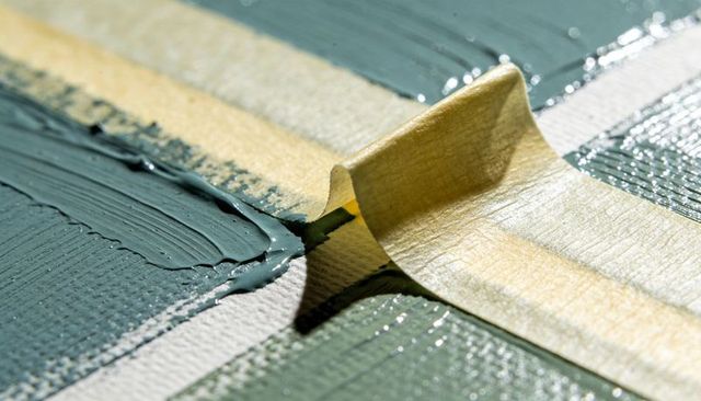 Peeling masking tape revealing crisp edge on wet emerald paint on stretched canvas macro closeup