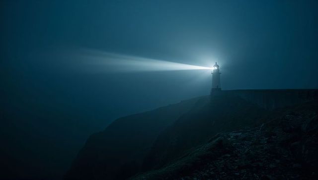 Lighthouse illuminating misty night ocean from rocky cliff