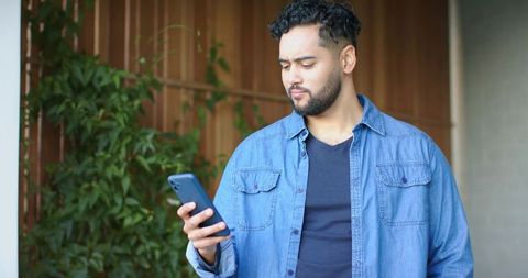 Young man standing on patio checking smartphone wearing denim shirt and dark tee