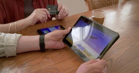 Diverse mature couple booking travel online using tablet and credit card at kitchen table