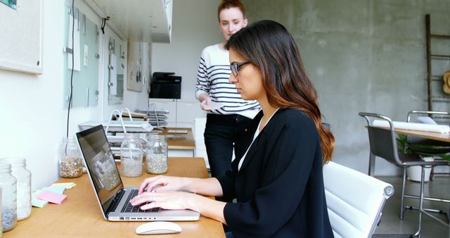 Woman Typing on Laptop While Colleague Discussing Documents - Download Free Stock Images Pikwizard.com